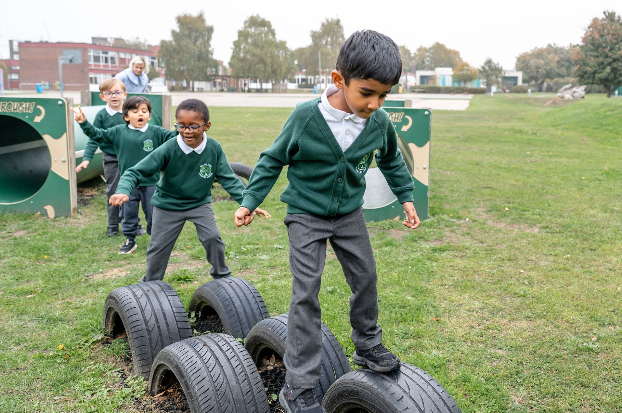 2 children balance on tyres on the school field